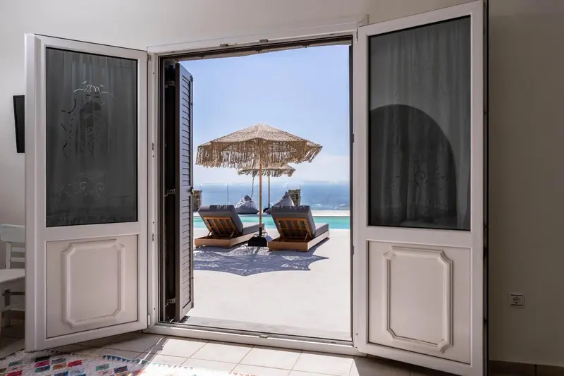 Une ouverture donne sur une terrasse avec des transats et un parasol face à la mer.