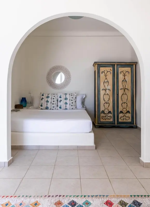 Une chambre lumineuse avec un lit fait et une armoire décorative.