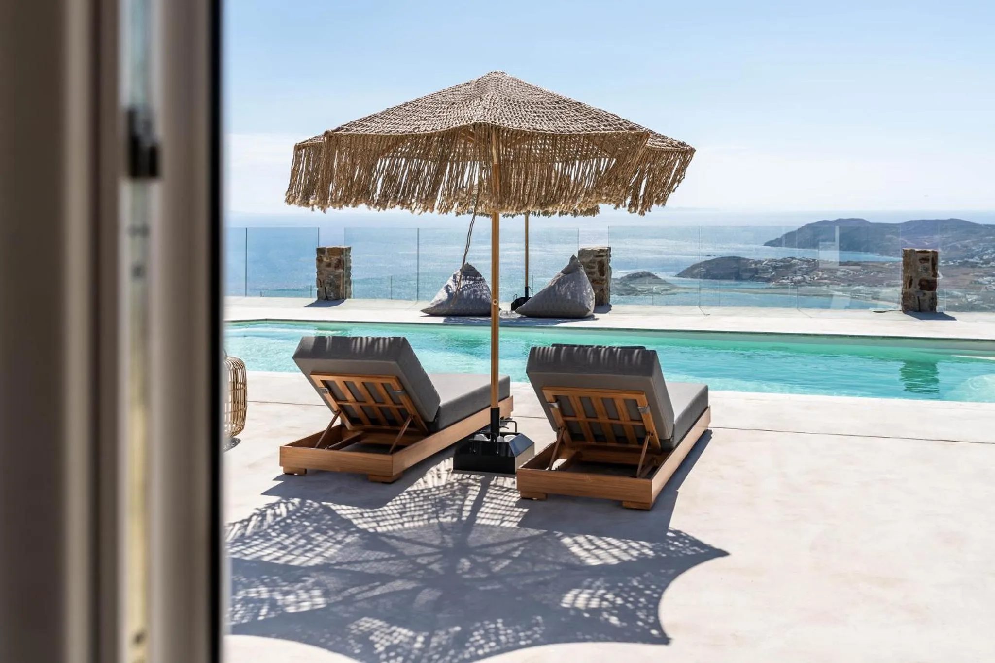 Deux transats et un parasol ombragent une terrasse avec piscine et vue sur la mer.