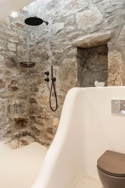 Une douche à l'italienne dans une salle de bain aux murs en pierre.