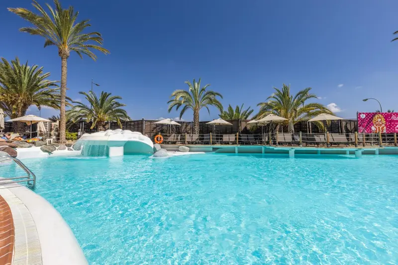 Piscine turquoise avec cascade artificielle et transats sous des parasols.