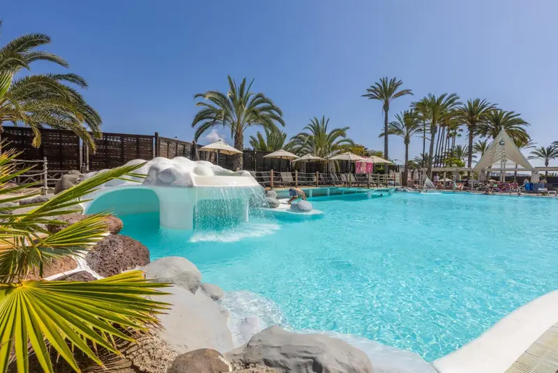 Une piscine turquoise avec une cascade rocheuse et des transats.