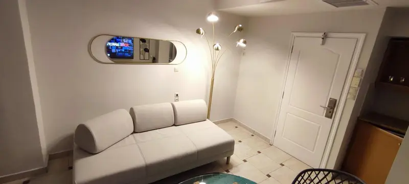 Un canapé blanc est placé devant un miroir ovale et une porte.