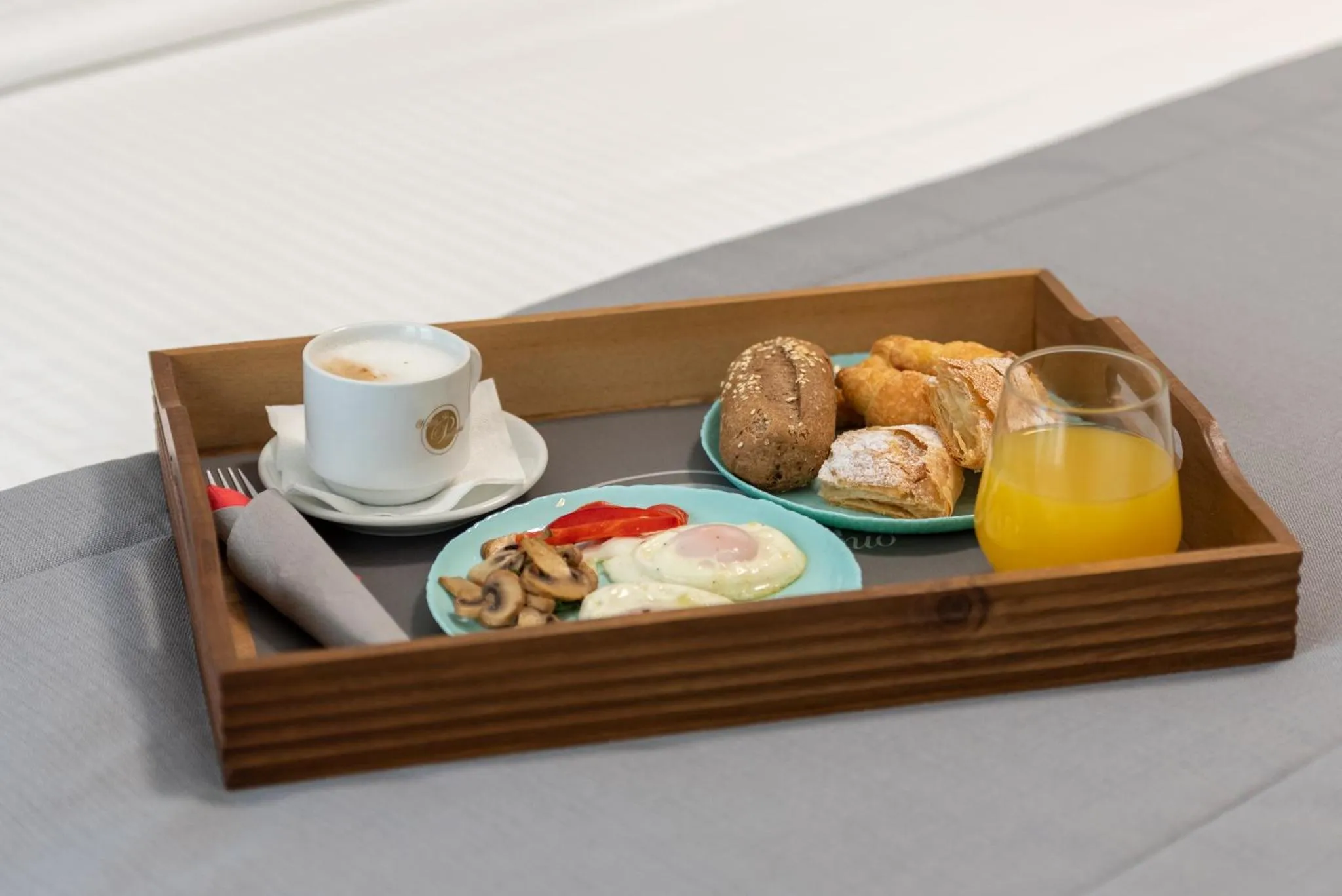 Un plateau de petit-déjeuner avec une boisson, des viennoiseries et une assiette d'œufs brouillés est présenté sur un lit.