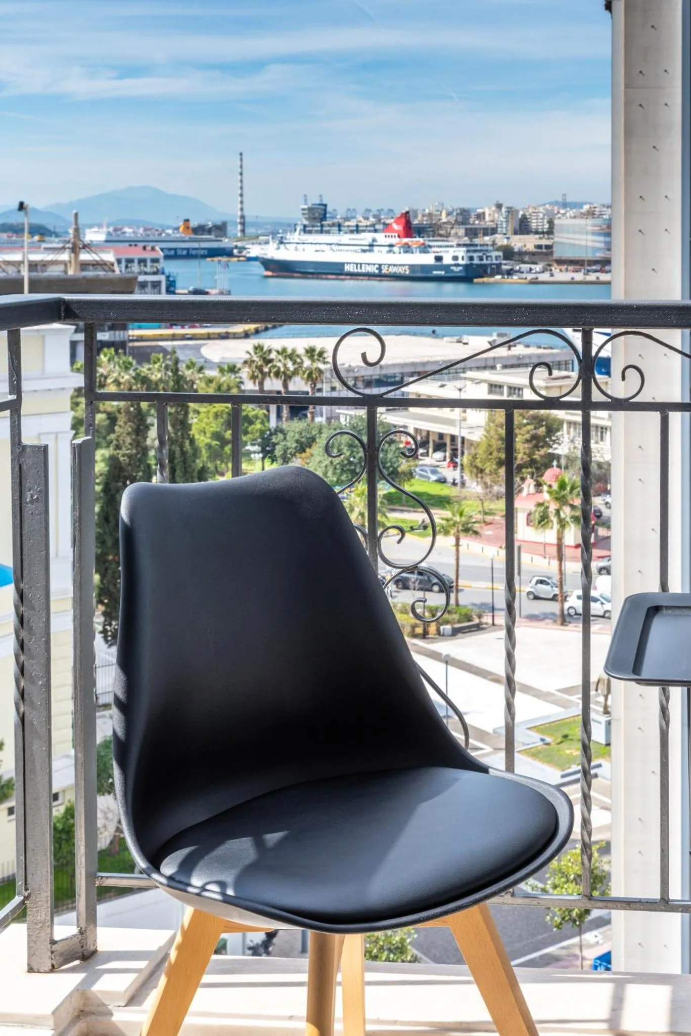 Une chaise en plastique noire sur un balcon avec vue sur la mer et la ville.