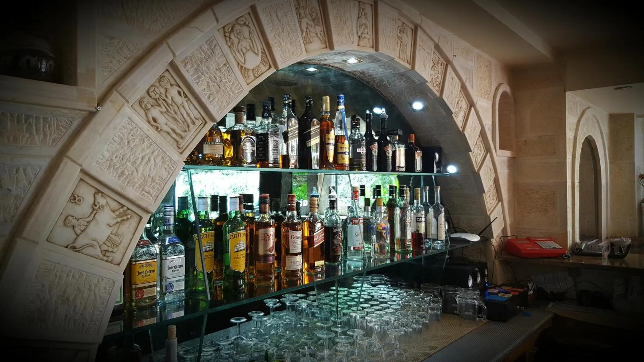 Un comptoir de bar illuminé présente une variété de bouteilles et de verres.