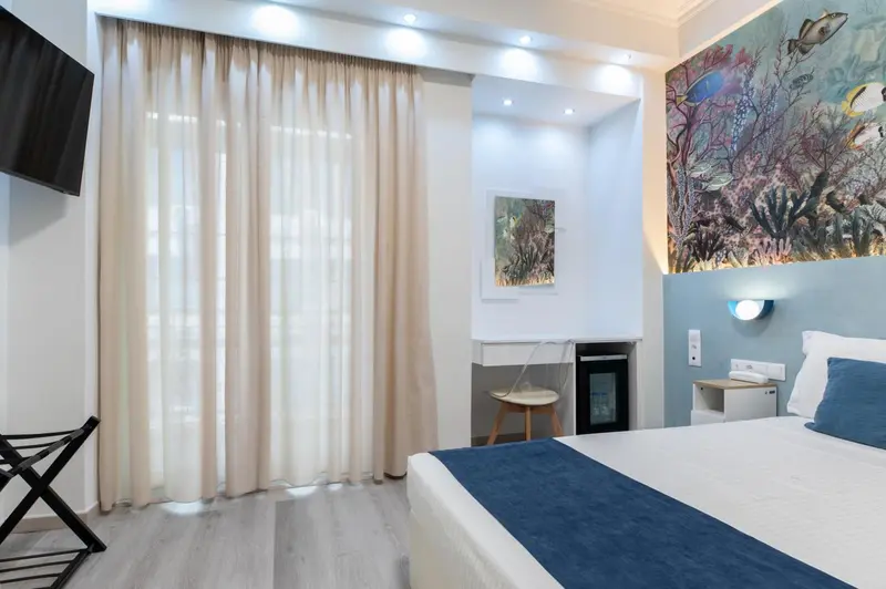Chambre lumineuse avec un lit recouvert d'une courtepointe bleue et un mur décoré d'une fresque marine.