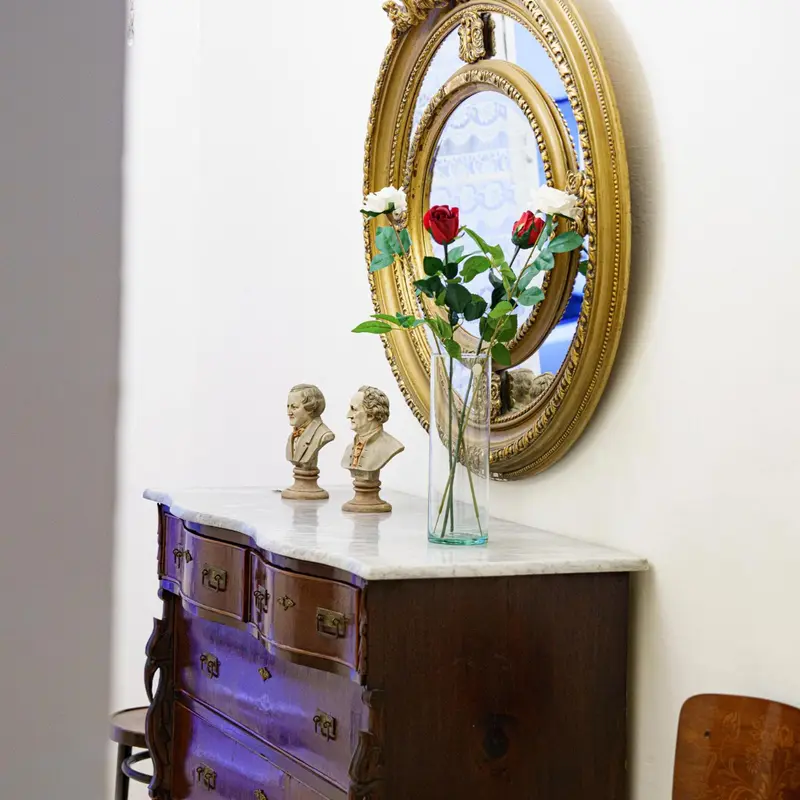 Une commode en bois ornée de bustes et surmontée d'un miroir avec des fleurs.