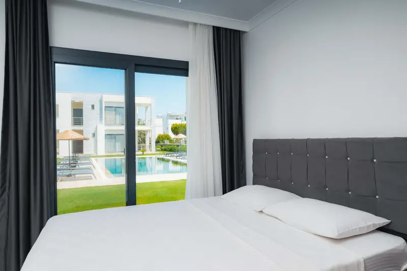Une chambre lumineuse avec un grand lit donnant sur une piscine et un jardin verdoyant.