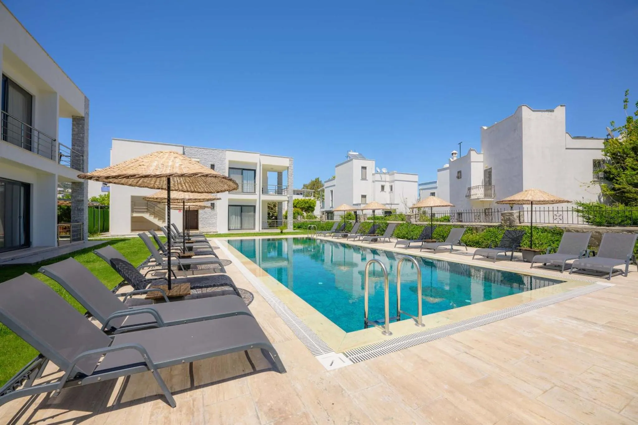 Transats et parasols bordent une piscine rectangulaire dans un espace extérieur soigné.