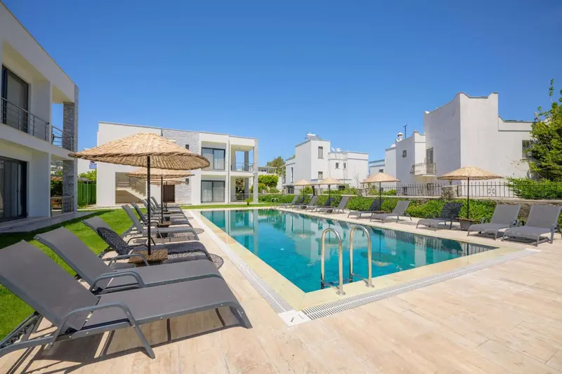 Transats et parasols bordent une piscine rectangulaire dans un espace extérieur soigné.