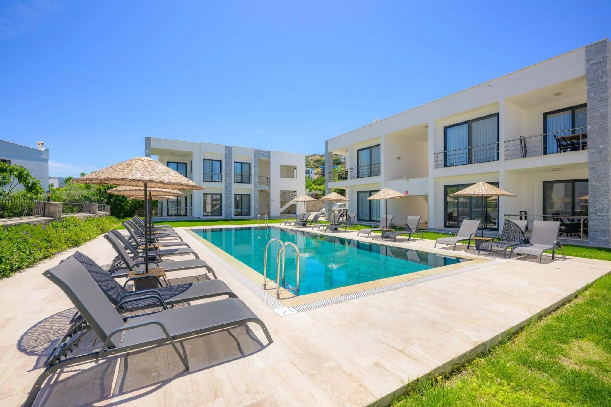 Transats et parasols bordent une piscine rectangulaire dans un jardin verdoyant.