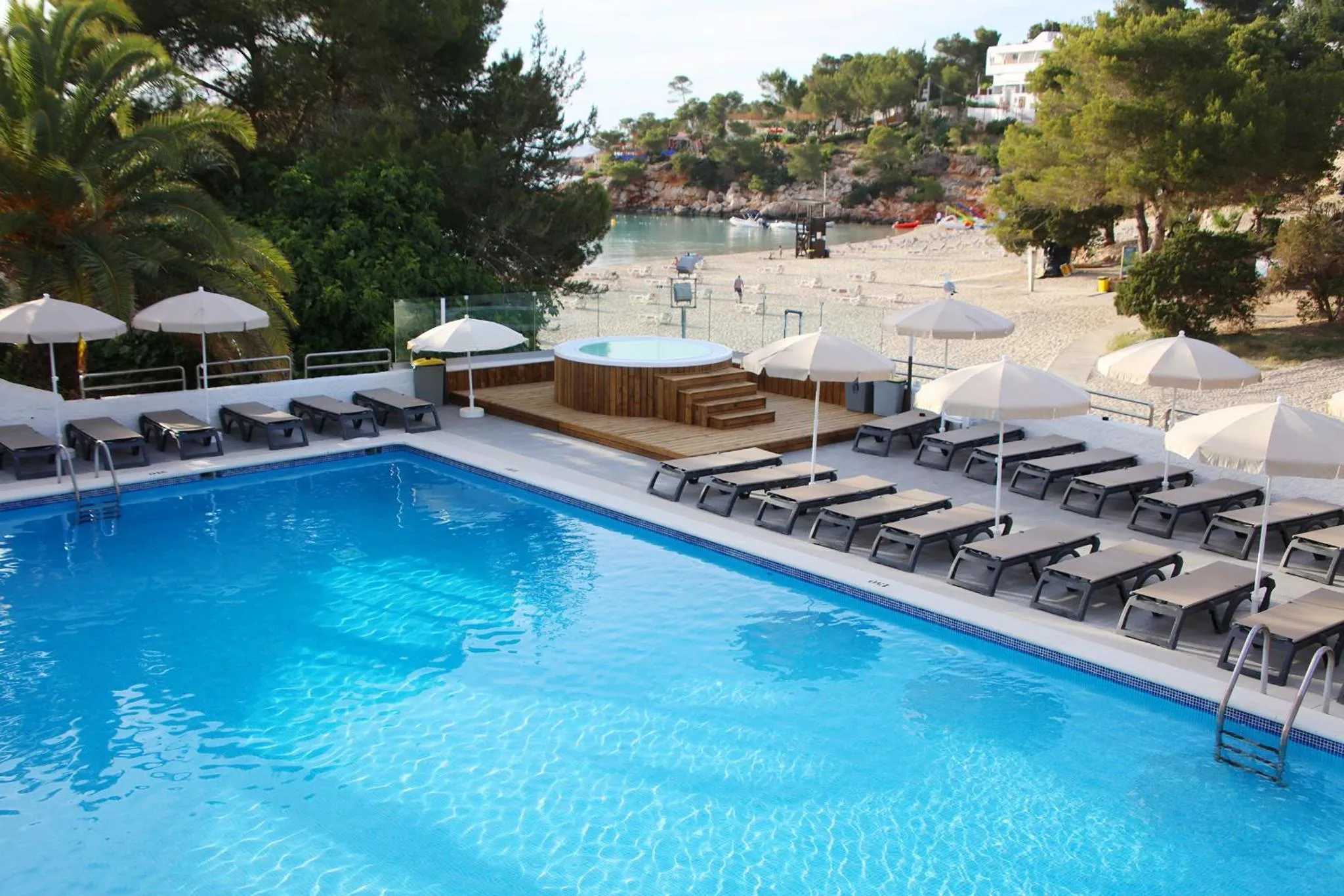 Terrasse avec jacuzzi et transats autour d'une piscine bleu clair.