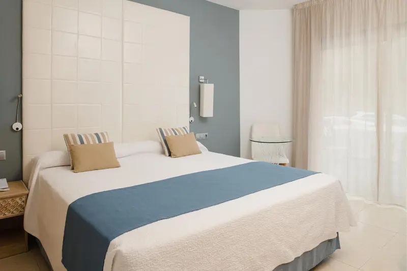 Une chambre lumineuse avec un grand lit recouvert d'une courtepointe bleue et de coussins.