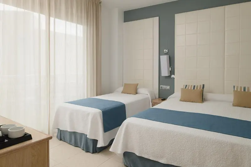 Chambre avec deux lits simples et une fenêtre voilée.
