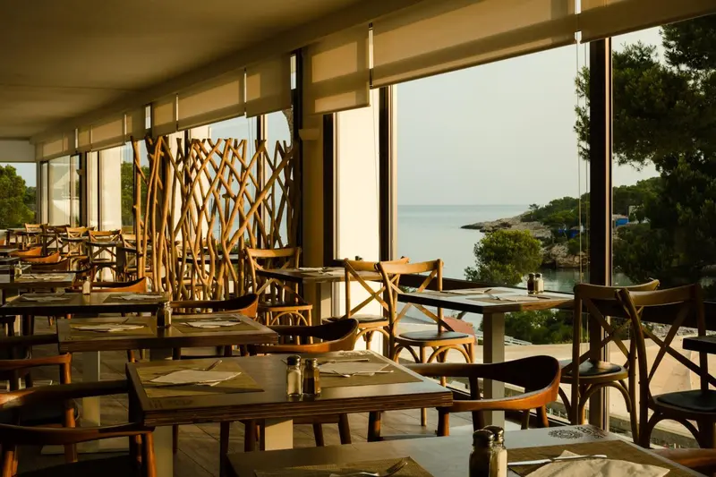 Une salle lumineuse avec des tables dressées face à la mer.