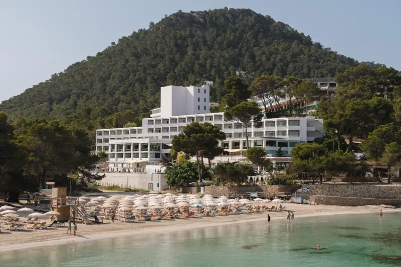 Bâtiment blanc moderne surplombant une plage de sable fin et une mer turquoise.