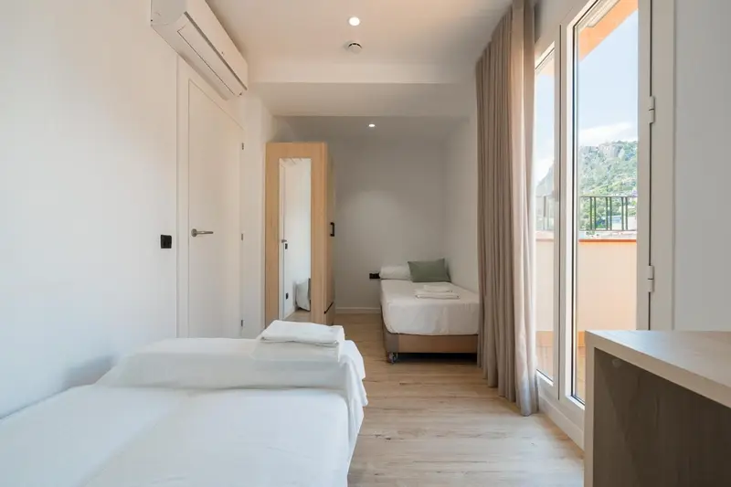 Chambre lumineuse avec deux lits simples et accès à un balcon.