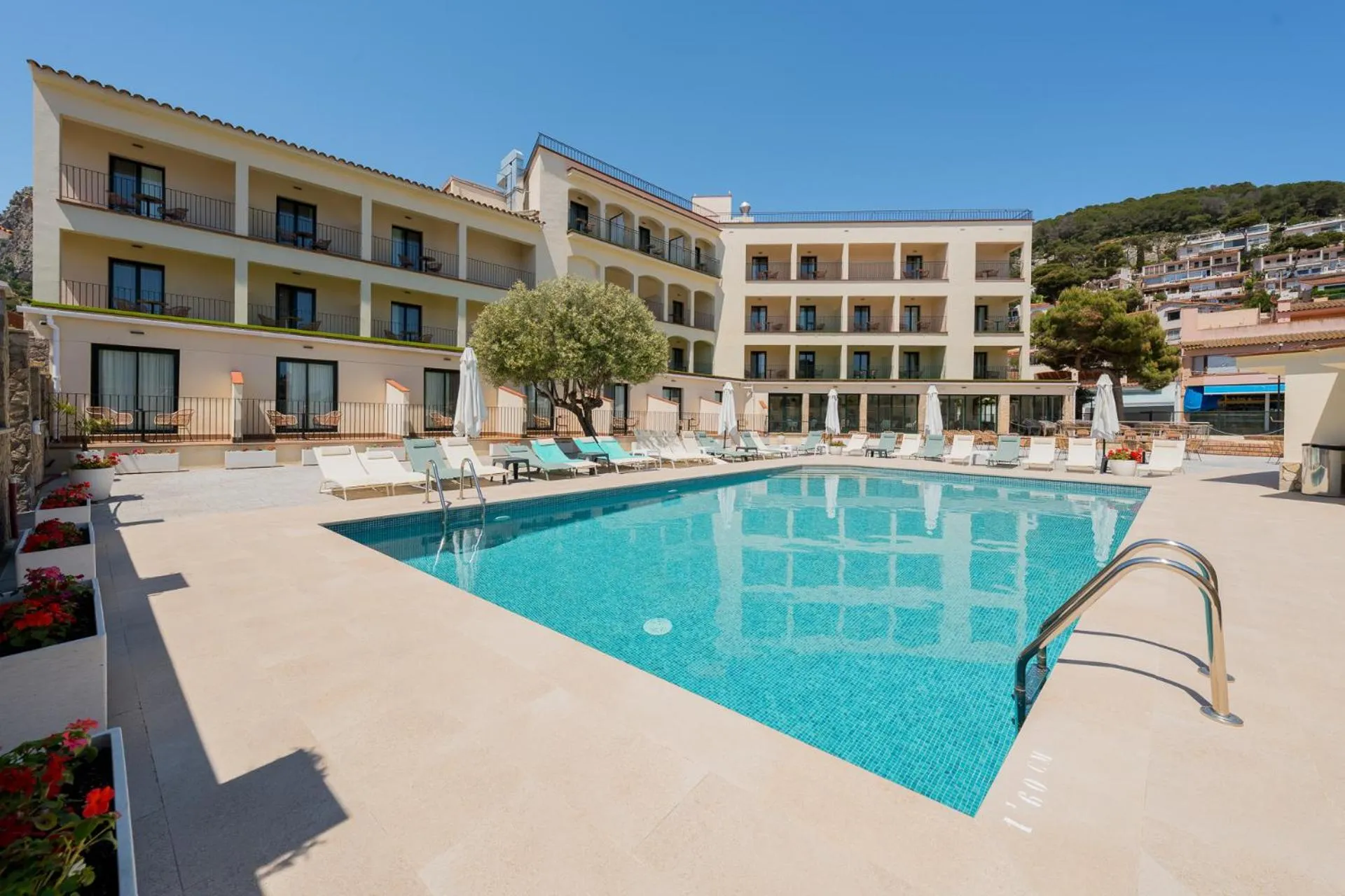 Bâtiment beige avec des balcons et une piscine rectangulaire entourée de chaises longues.