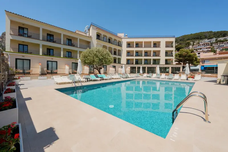 Bâtiment beige avec des balcons et une piscine rectangulaire entourée de chaises longues.