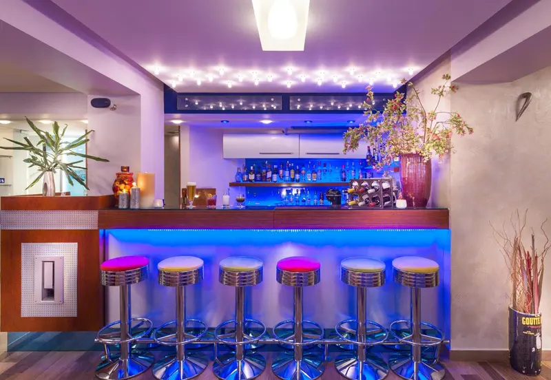 Un comptoir de bar illuminé avec des tabourets hauts et des bouteilles.