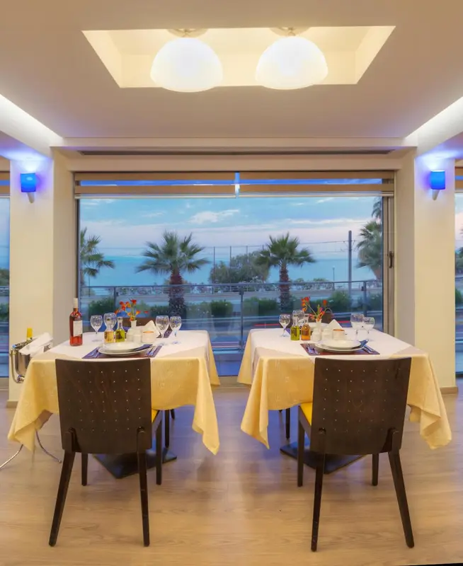 Une table est dressée devant une grande baie vitrée donnant sur la mer.