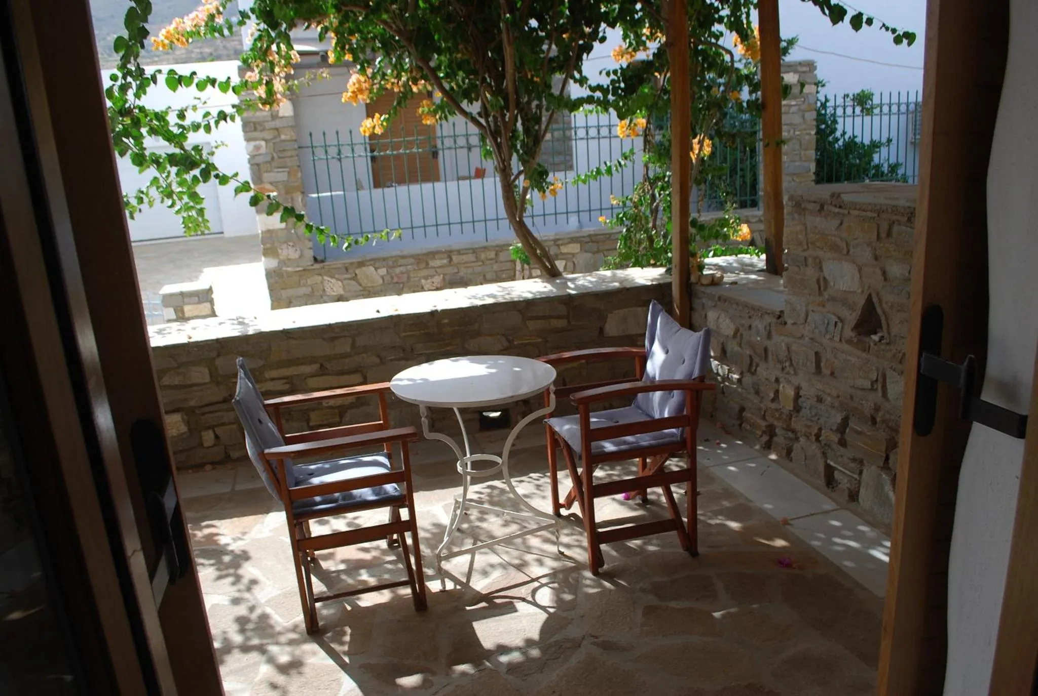 Terrasse ombragée avec table et chaises en fer forgé.
