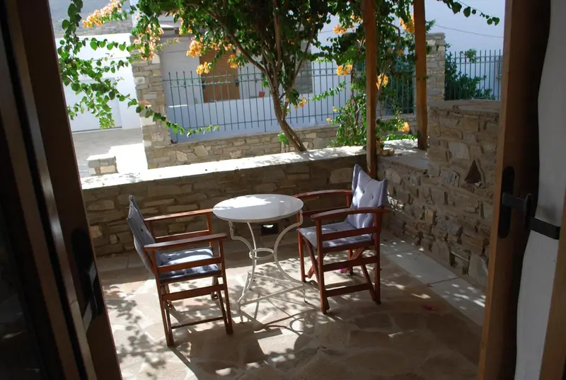 Terrasse ombragée avec table et chaises en fer forgé.