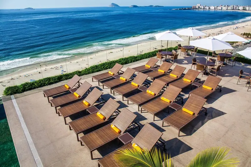 Terrasse aménagée avec transats et tables offrant une vue sur la plage et la mer.
