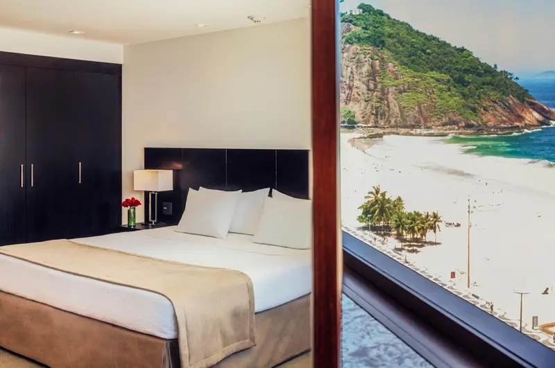 Une chambre avec un grand lit face à une baie vitrée donnant sur une plage.