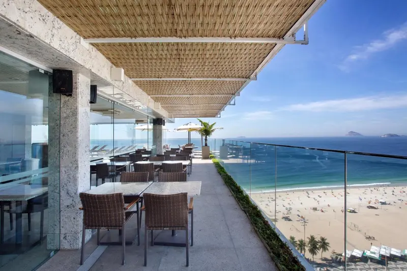 Terrasse ombragée avec tables et chaises donnant sur une plage.