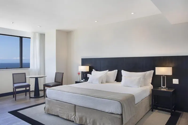 Une chambre lumineuse avec un grand lit et un coin salon près de la fenêtre.
