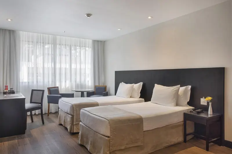 Une chambre d'hôtel lumineuse avec deux lits simples et un coin salon.