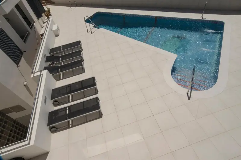 Vue aérienne d'une piscine rectangulaire entourée d'une terrasse carrelée avec des transats.