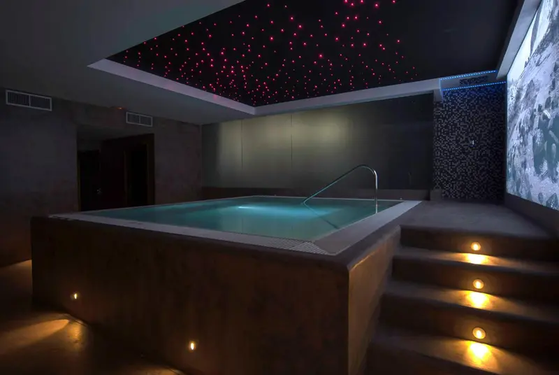 Un jacuzzi rectangulaire intégré dans un espace sombre et moderne.