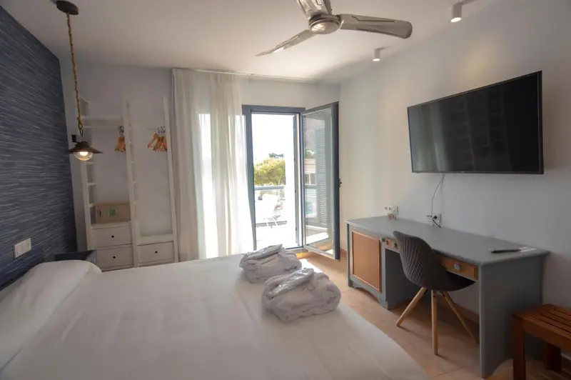 Une chambre lumineuse avec un grand lit et un bureau près d'une baie vitrée.
