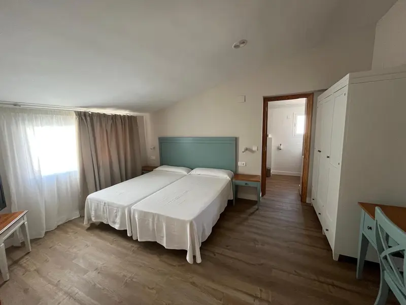 Une chambre lumineuse avec deux lits simples et une armoire.