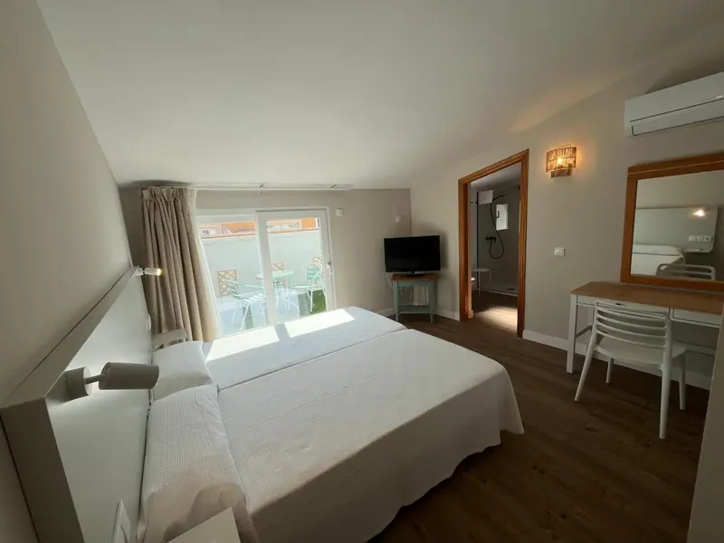 Une chambre lumineuse avec un lit blanc et un bureau.