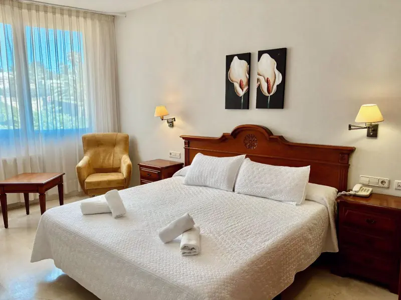 Une chambre lumineuse avec un grand lit et un fauteuil.