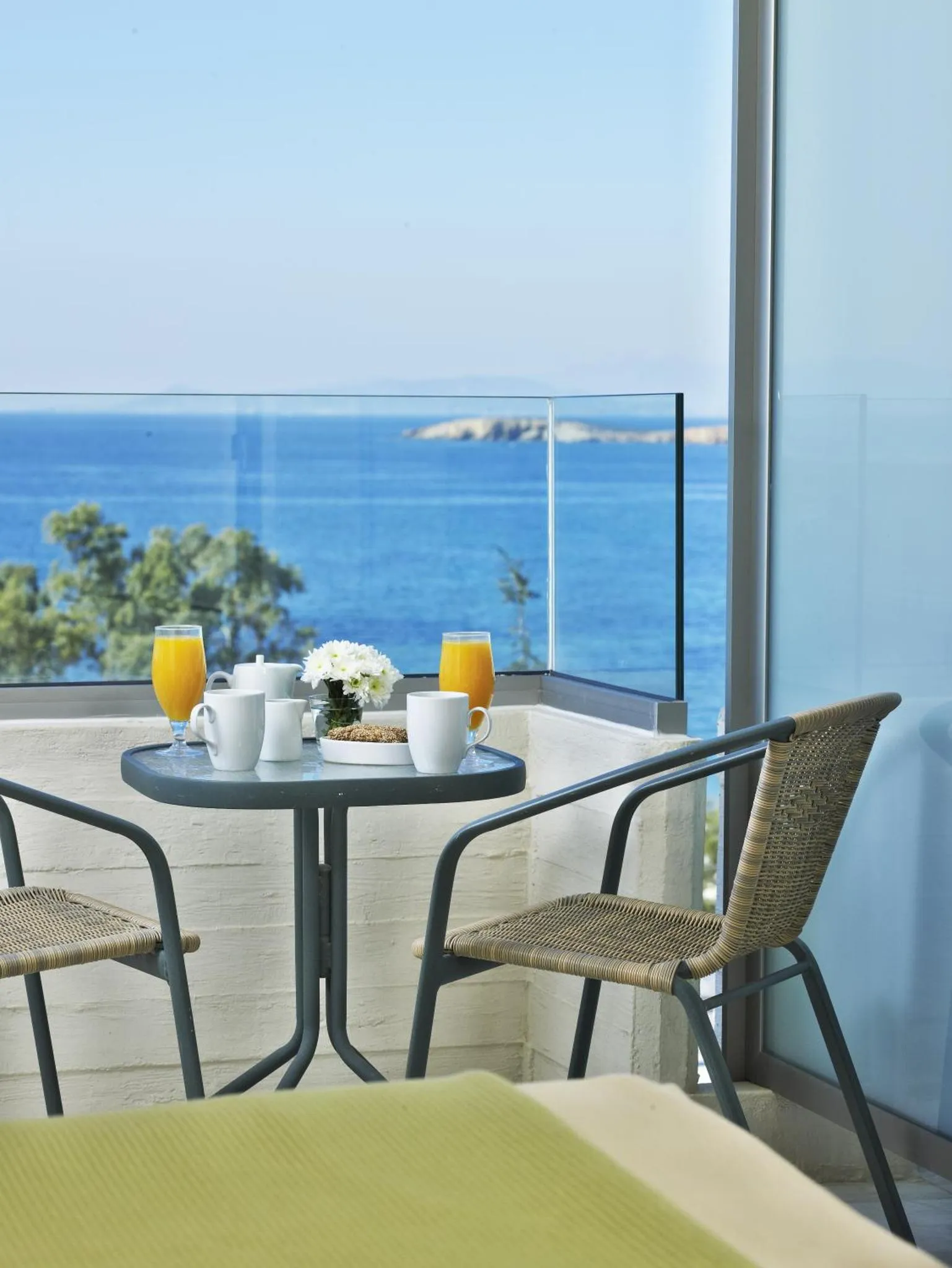 Une table avec des boissons et des pâtisseries est mise en scène sur un balcon avec vue sur la mer.