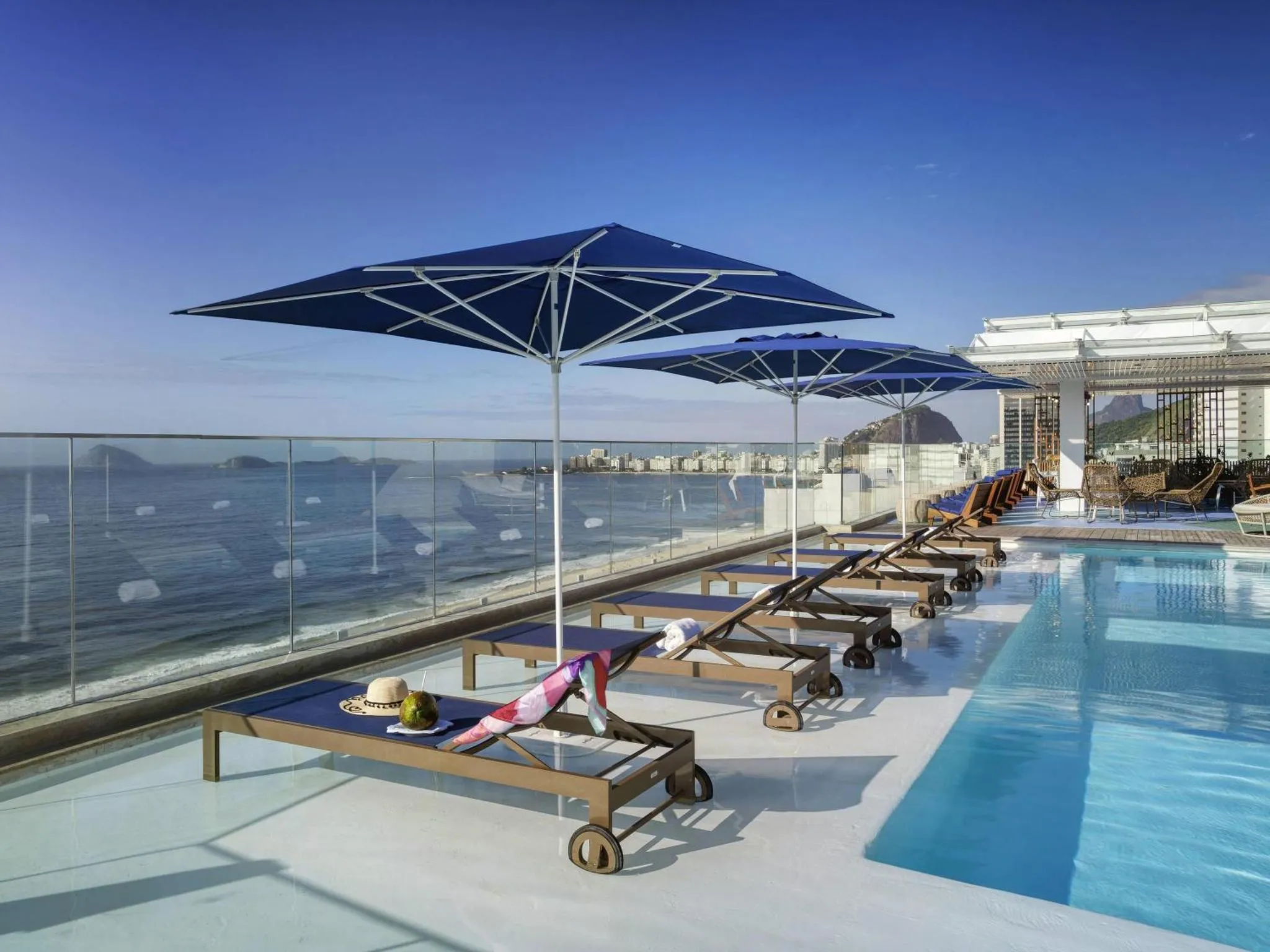 Transats bleus et parasols sur une terrasse avec piscine et vue sur la mer.