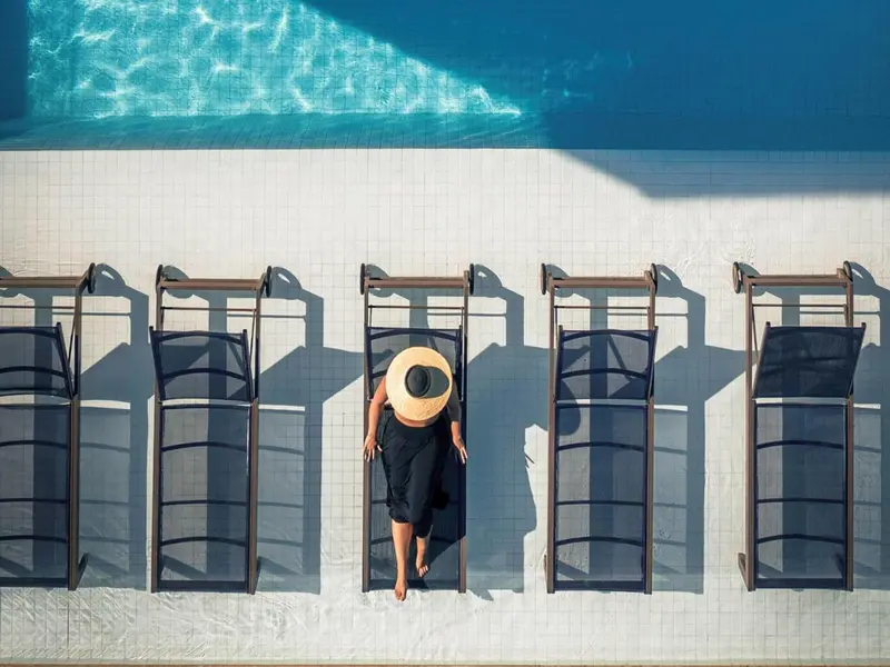 Vue aérienne d'une piscine avec des chaises longues et une personne portant un chapeau.