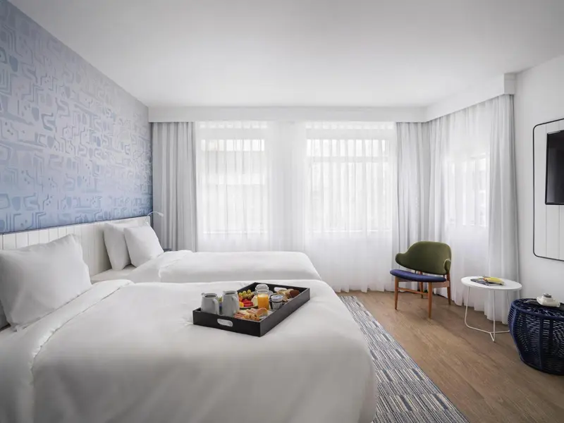 Une chambre lumineuse avec deux lits simples et un plateau de petit-déjeuner.