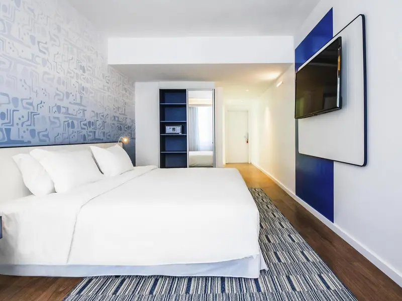 Une chambre lumineuse avec un grand lit et une télévision murale.