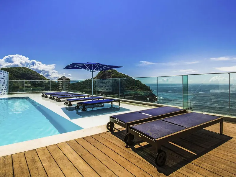 Transats bleus alignés au bord d'une piscine sur une terrasse ensoleillée avec vue sur la mer.