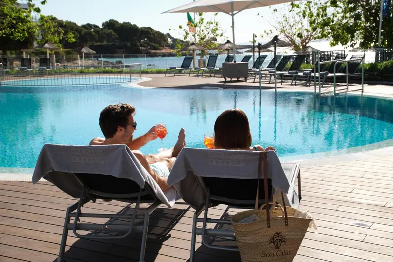 Deux personnes se relaxent au bord d'une piscine ensoleillée.