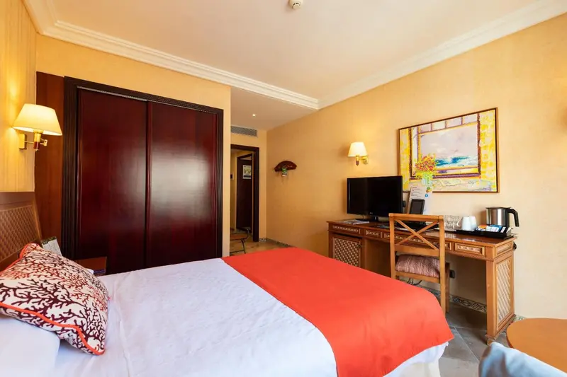 Une chambre d'hôtel lumineuse avec un lit recouvert d'une couverture rouge et un bureau en bois.