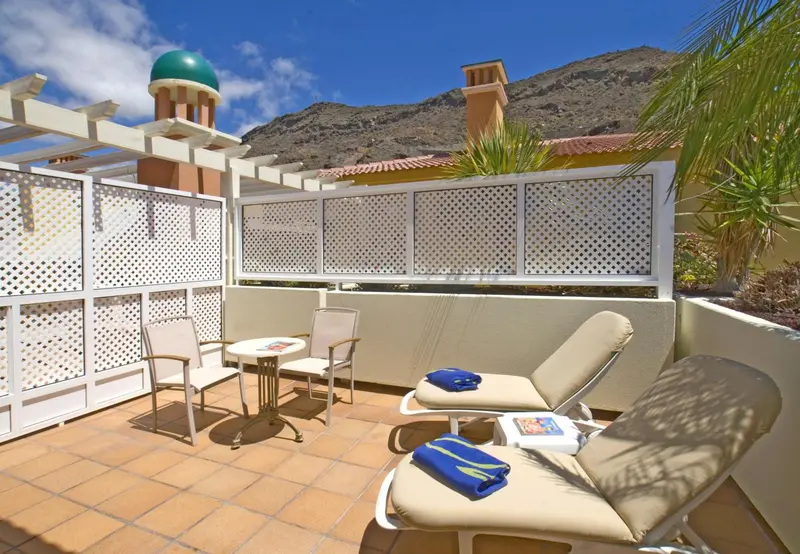 Terrasse carrelée avec mobilier de détente et pergola ombragée.