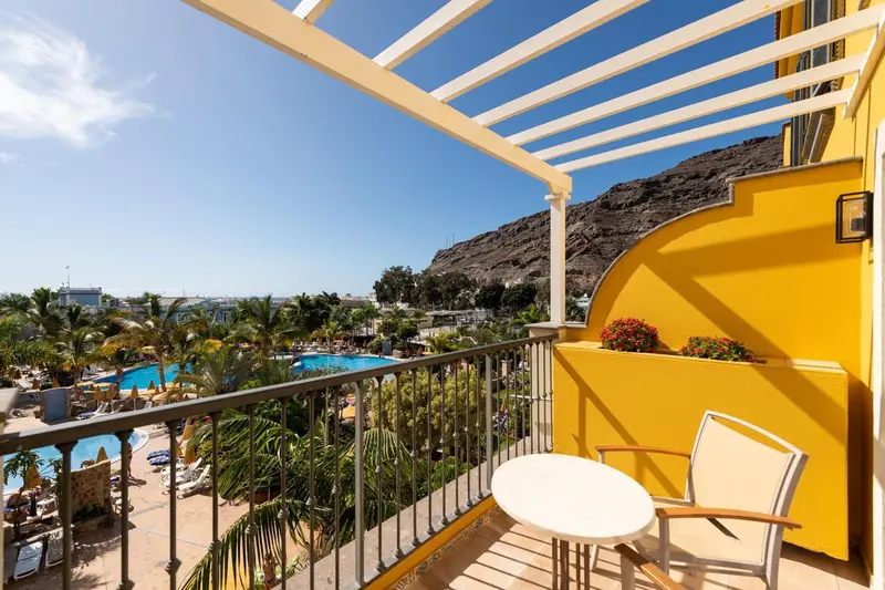 Terrasse ensoleillée donnant sur une piscine et un paysage montagneux.