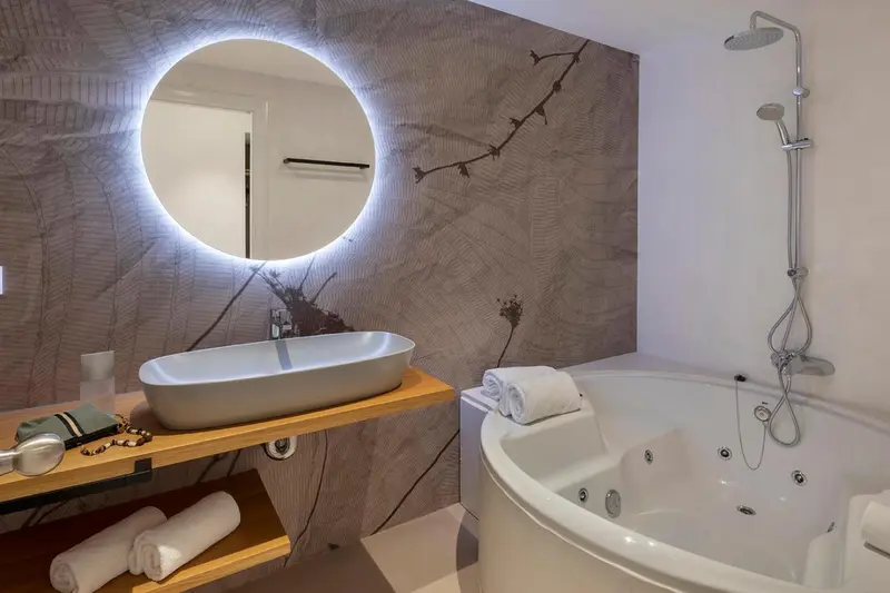 Une salle de bain moderne avec une baignoire d'angle et un grand miroir rond.